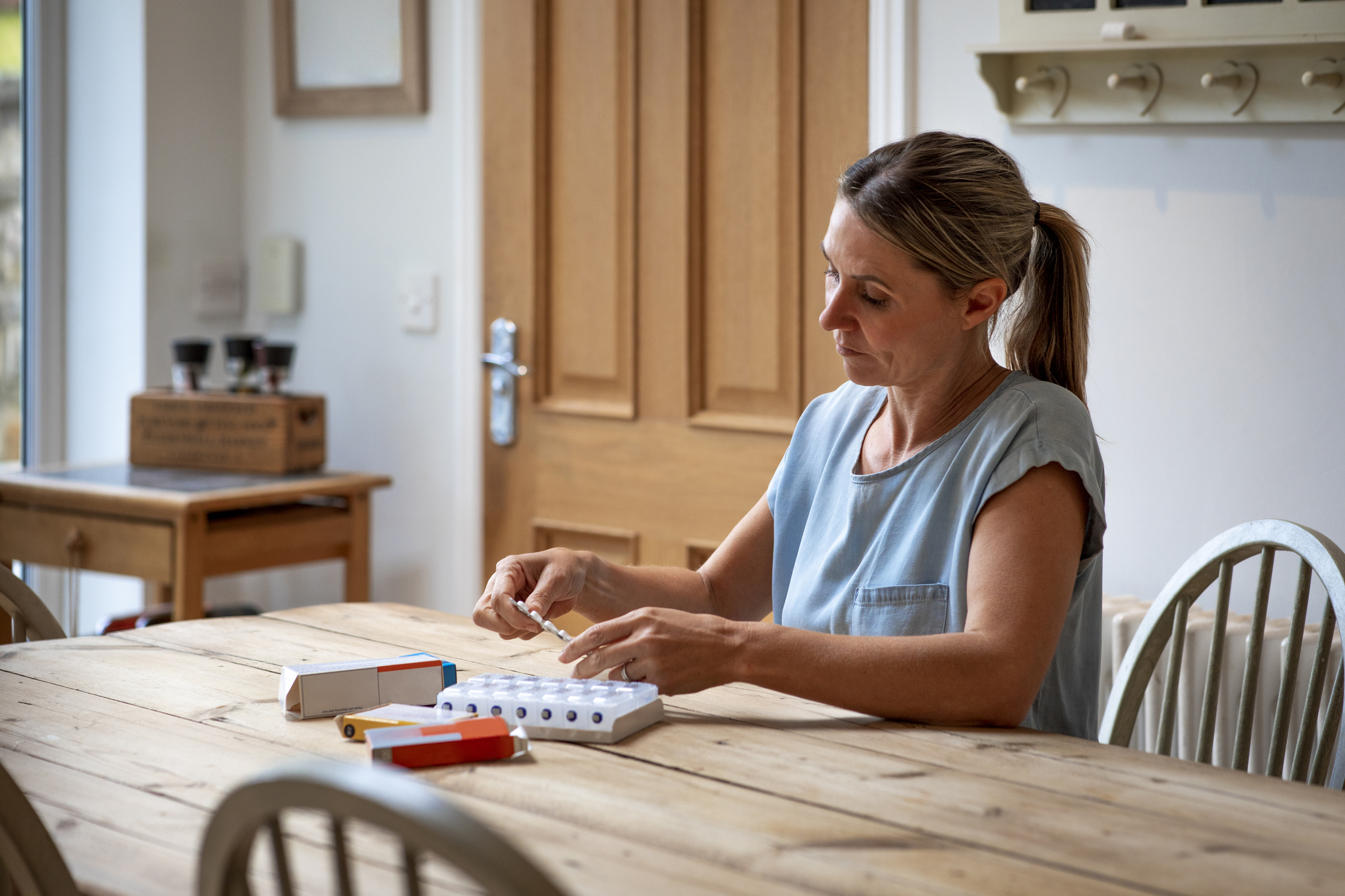 Woman organizing her medication into a weekly pill organizer at home