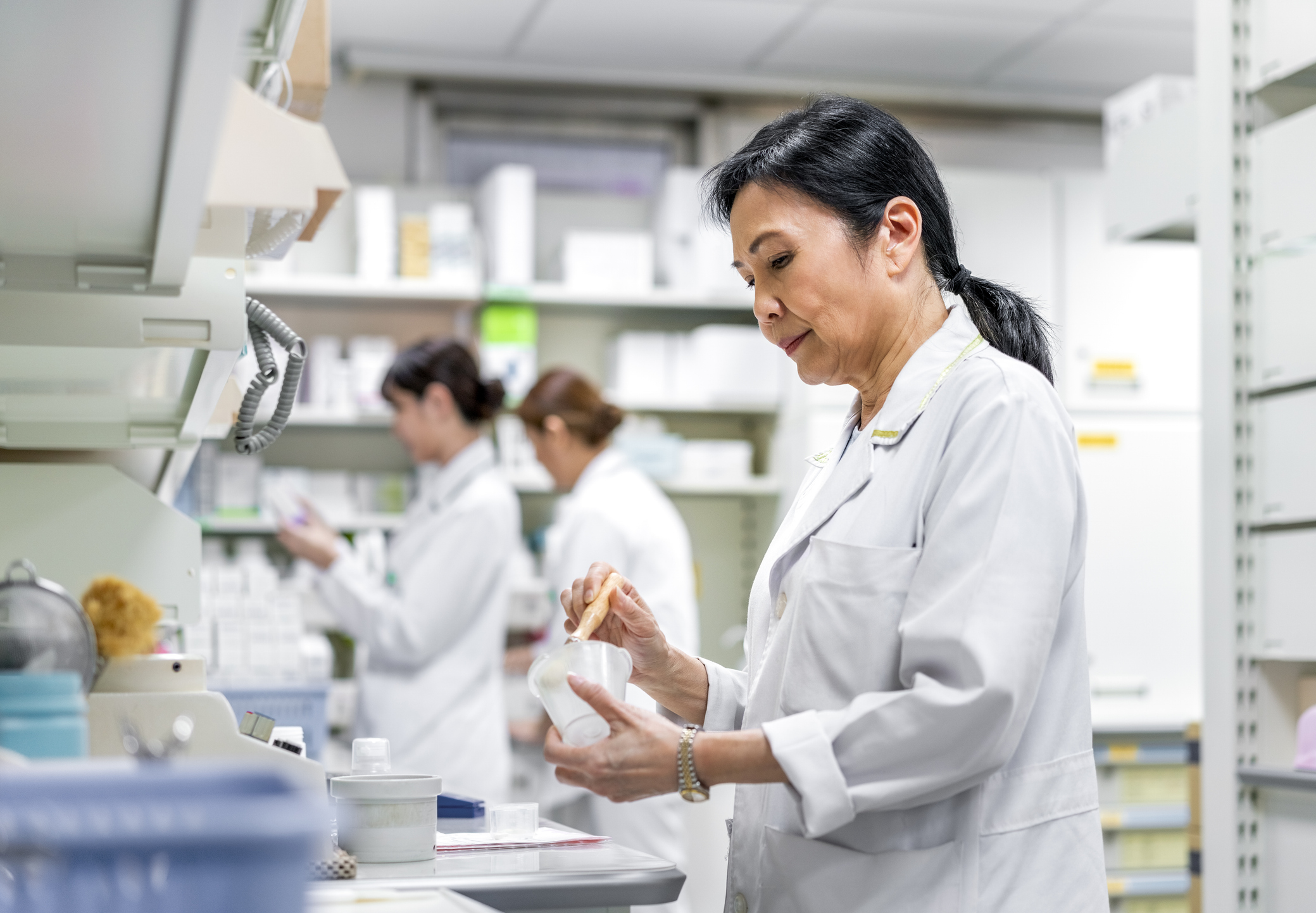 Pharmacist in a white coat compounding medication at a pharmacy